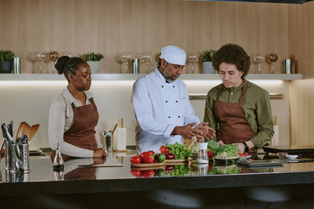 Professional chef in white uniform telling cooking plant and demonstrating all ingredients while interns watching his actionの写真素材