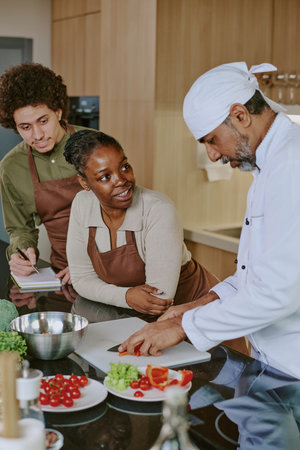 Biracial apprentices watching Indian chefs cutting vegetable during cooking courseの写真素材
