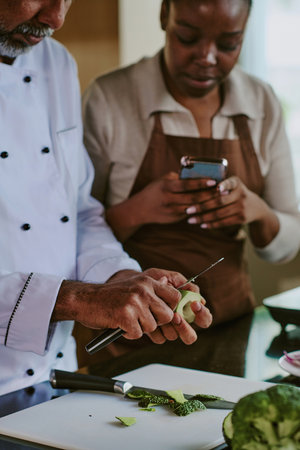 Vertical shot of unrecognizable professional chef peeling fresh avocado while his sous chef recording video of processの写真素材