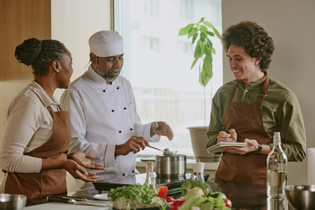 Chef cooking special sauce while his biracial interns discussing recipe with him togetherの写真素材