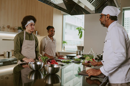 Chef explaining recipe details to his cooks who listening him and ready to cook dishの写真素材