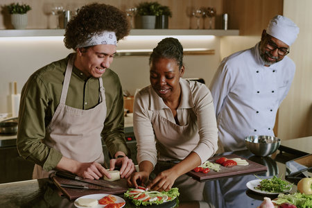 Young sous chef and African American female cook making caprese appetizer together while mature Indian chef controlling themの写真素材