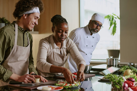 African American female cook decorating caprese appetizer while curly haired sous chef and Indian chef watching her actionsの写真素材