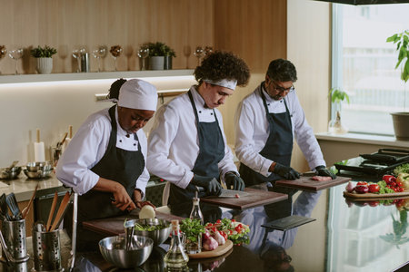 High angle shot of multiracial professional cooking team cutting ingredients on wooden cutting board in modern spacious kitchenの写真素材