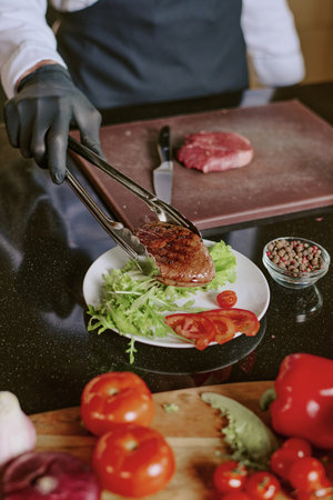 Vertical high angle shot of unrecognizable cooks hands serving dish with grilled beef steakの写真素材