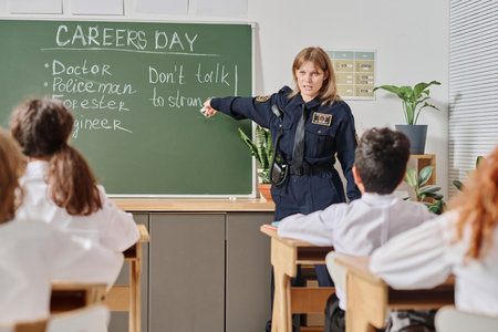 Female police officer standing at blackboard in front of class working with group of kids on career guidance dayの写真素材