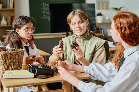 Caucasian female forester showing pine and cedar cones to teenagers while giving information about her job during classの写真素材