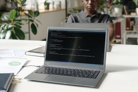 Medium close up of silver laptop with codes on black screen in modern officeの写真素材