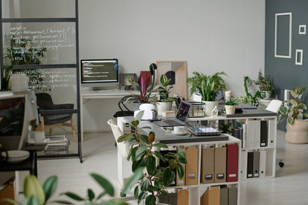 Fully equipped modern office with several workspaces and huge number of verdant plantsの写真素材