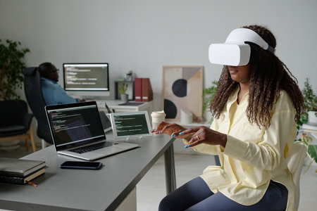 African American office worker with VR headset sitting at table and imitating typing on invisible keyboardの写真素材