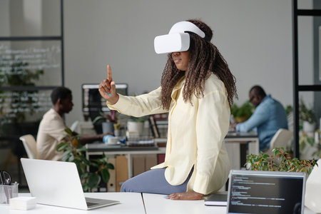 Curly haired woman playing video game while sitting on work table with laptopsの写真素材