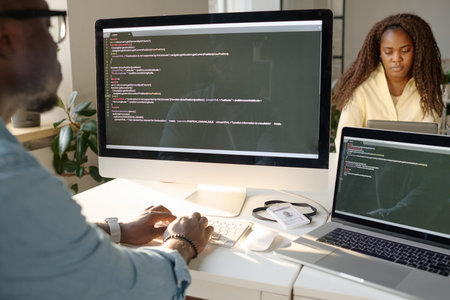 Unrecognizable man sitting at table and looking at computer screen while codingの写真素材