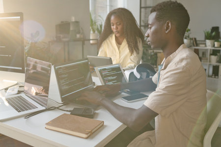 African American man and woman working together in coworking zone, photo illuminated by sunの写真素材