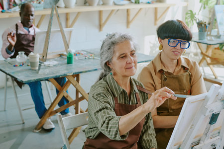 High angle shot of group of senior people drawing with oils paints on canvas while their young female teacher watching themの写真素材