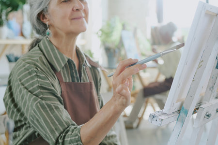 Medium close up of hand of senior Caucasian woman holding brush while doing strokes on white canvasの写真素材