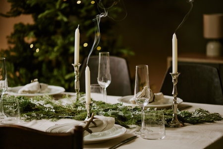 Medium close up extinguished candles in silver candlesticks on table decorated with pine garlands...