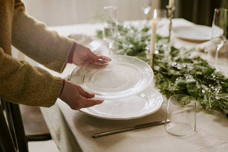 Medium close up of unrecognizable woman putting transparent crystal plate on table while serving...
