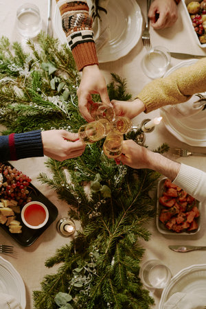 Top down shot of unrecognizable friends sitting at decorated for X-mas table and clinking crystal...