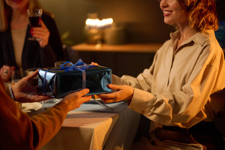 Medium close up of unrecognizable boyfriend giving gift covered in blue gift wrapping to his beloved lover who smiling widelyの写真素材