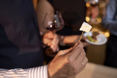 High angle shot of unrecognizable male hands holding piece of camembert on toothpick and wine glassの写真素材