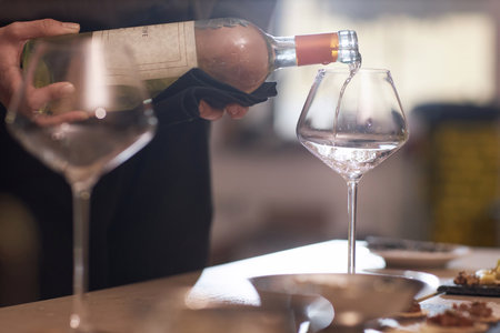Medium close up of unrecognizable female holding bottle of white wine and pouring into perfect crystal glassの写真素材
