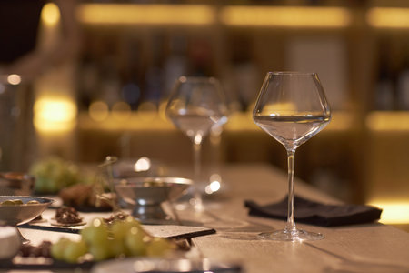 Polished crystal glass with white wine on table served with appetizers for wine degustation in dimly lit roomの写真素材