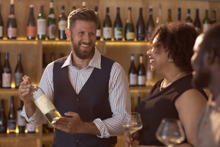 Smiling Caucasian wine expert demonstrating unique bottle of white wine to sommeliers with wine glasses in hands and smile on facesの写真素材