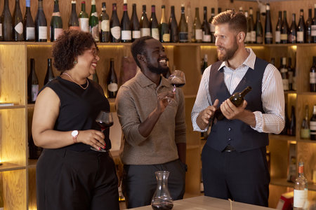 Biracial company of sommeliers tasting aged red wine and telling funny jokes, they having fun togetherの写真素材
