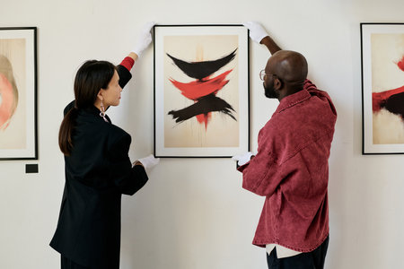 A woman and a man are examining a framed abstract painting displayed on a gallery wall, showcasing an appreciation for contemporary art in a thoughtful settingの写真素材