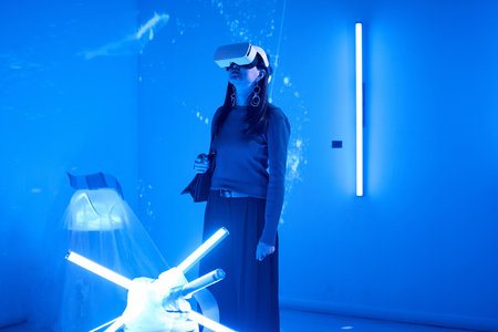 Person using virtual reality headset in a blue-lit futuristic room with modern lighting features and advanced technology setup creating an immersive environmentの写真素材