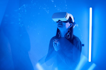 Woman immersed in virtual reality environment while using headset and accessories indoors...