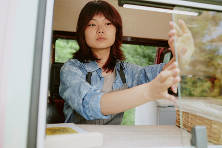 Medium close up of Asian woman in uniform closing van windowの写真素材