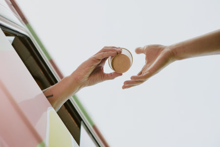 Low angle shot of unrecognizable worker hands giving paper coffee cup with hot beverage to unrecognizable customerの写真素材