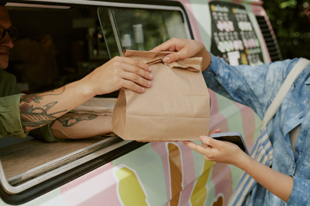 Medium close up of paper bag with order in hands of unrecognizable male cook and female customerの写真素材