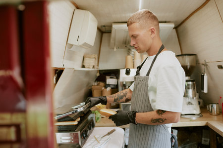 Side view of professional young adult cook opening grill to prepare hot dog bunsの写真素材
