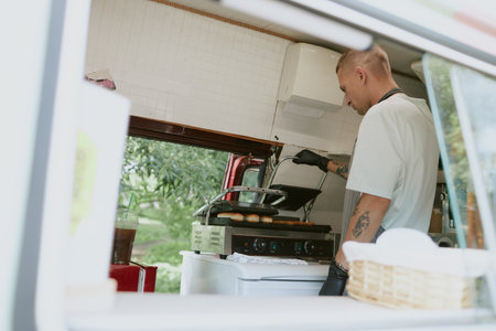 Back view shot of young adult chef checking sausages and buns for hot dogs on grillの写真素材