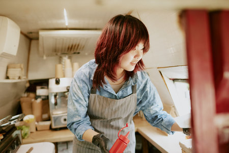 Asian female chef with ketchup squeeze bottle in hand taking order with light smile on faceの写真素材