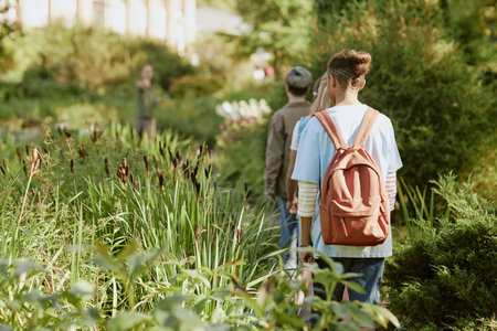 Rear view shot of unrecognizable teenagers walking along path during excursion in botanical garden on sunny dayの写真素材