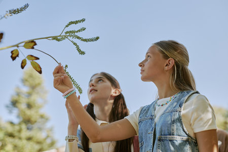 Low angle view of two teen girls looking closer at plant while walking along botanical gardenの写真素材