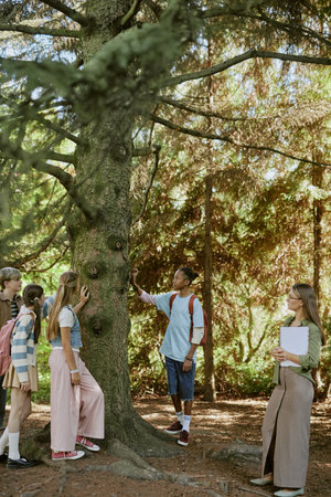 Vertical wide shot of teenagers touching old tree trunk during educational tour in botanical garden, copy spaceの写真素材