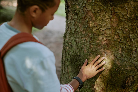 High angle view of Black teenager touching surface of old tree trunk in local park or botanical gardenの写真素材