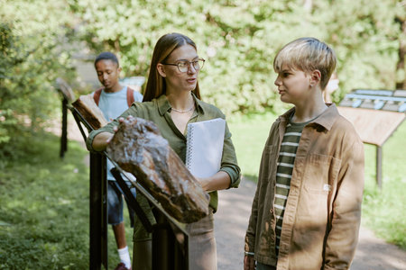 Young female botanical garden worker showing petrified wood while conducting tour for teen studentsの写真素材