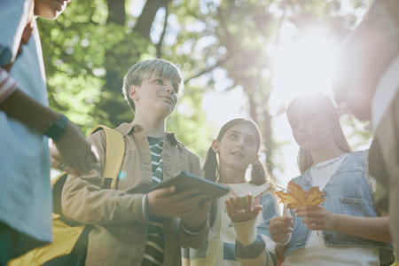 Low angle view of teenagers using digital tablet and talking to their teacher during outdoors class