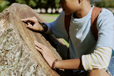 Medium section of African American boy wearing backpack counting old tree stump rings in local parkの写真素材