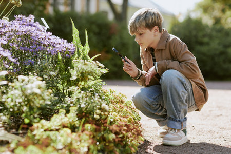 Curious Caucasian teen boy holding magnifying glass looking closer at flowers while studying plants in local park, copy space, side viewの写真素材
