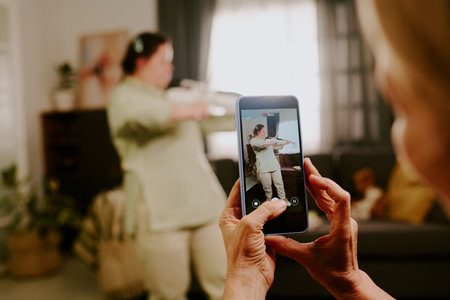 Unrecognizable mother recording video of her daughter with Down syndrome playing violin in living roomの写真素材