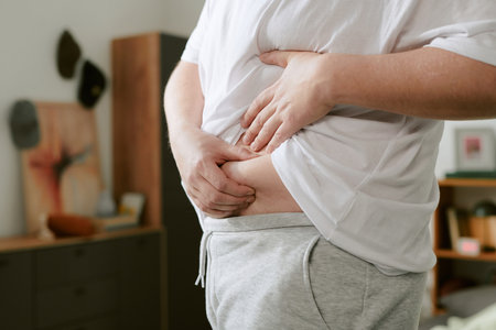 Close-up of person pulling up shirt to examine waistline in a cozy indoor setting. Dresser and artwork visible in background adding a homey touchの写真素材