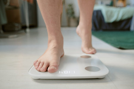Person standing on digital scale with visible weight readout in home setting. Background features household objects and furniture, emphasizing cozy atmosphereの写真素材