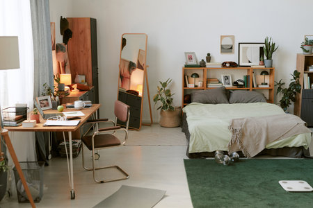Cozy modern bedroom featuring a neatly organized desk area with shelves, a comfortable bed, and stylish decor elements creating a serene and functional living spaceの写真素材