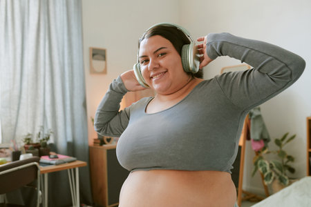 Portrait of smiling woman wearing headphones, listening music in cozy, warmly-lit room decorated with plants and furnitureの写真素材